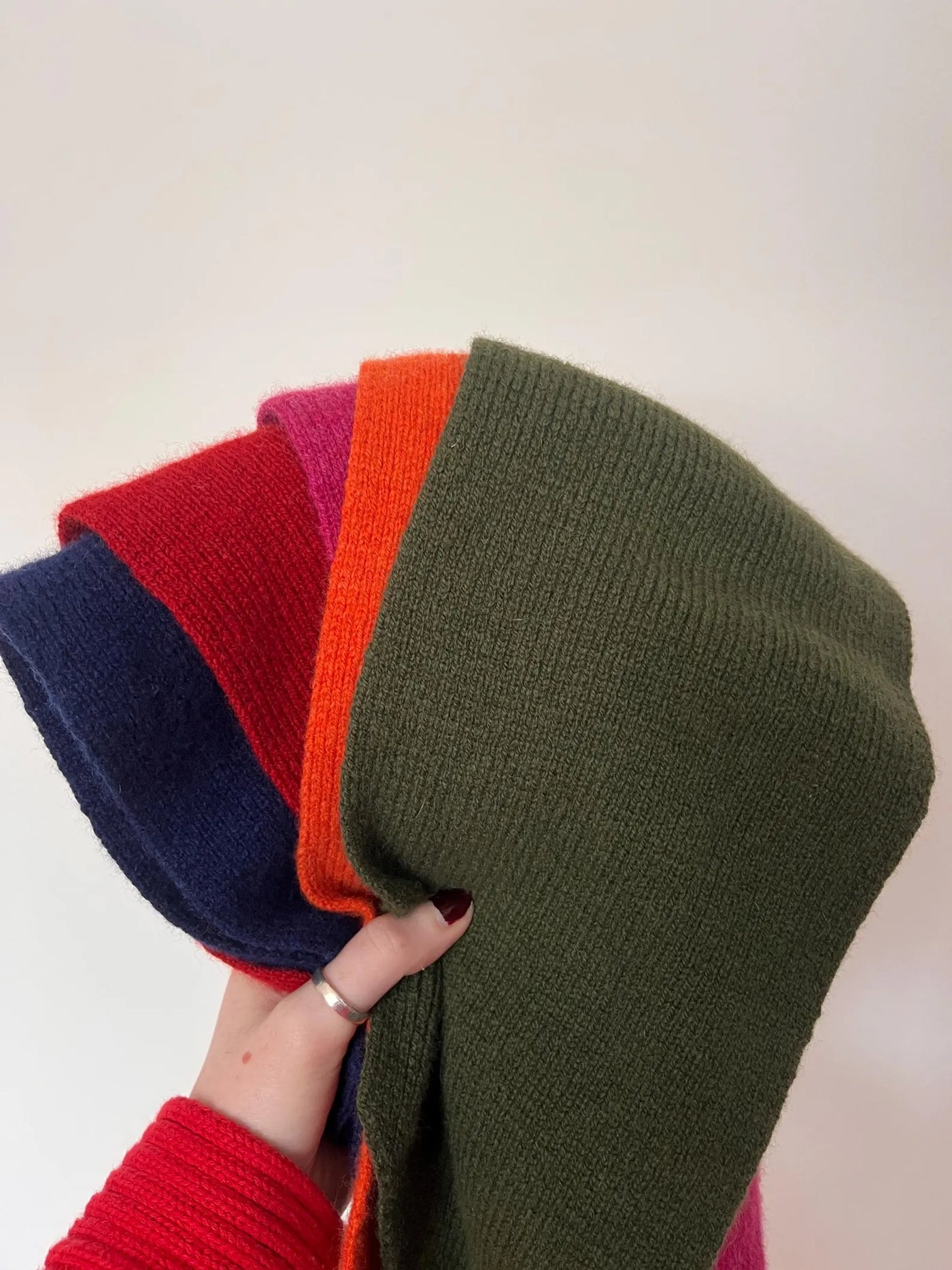 Stack of colorful knit hats held by a hand against a white background