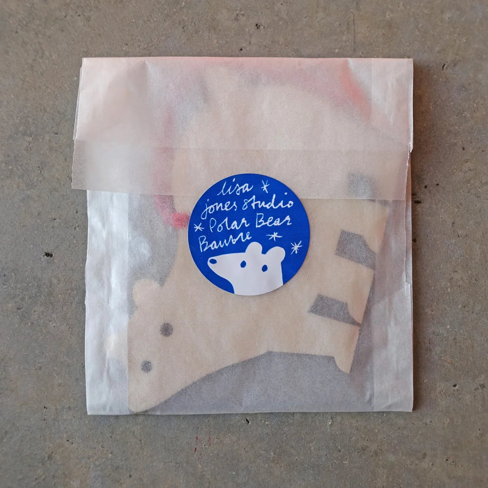 Polar bear baby bootie in a clear bag with a blue label on a gray background