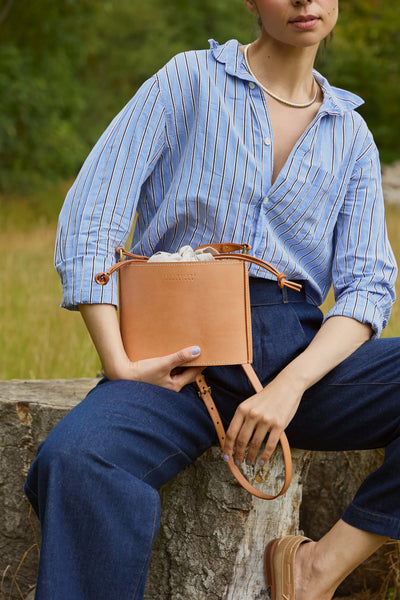 Person holding a brown leather bag outdoors