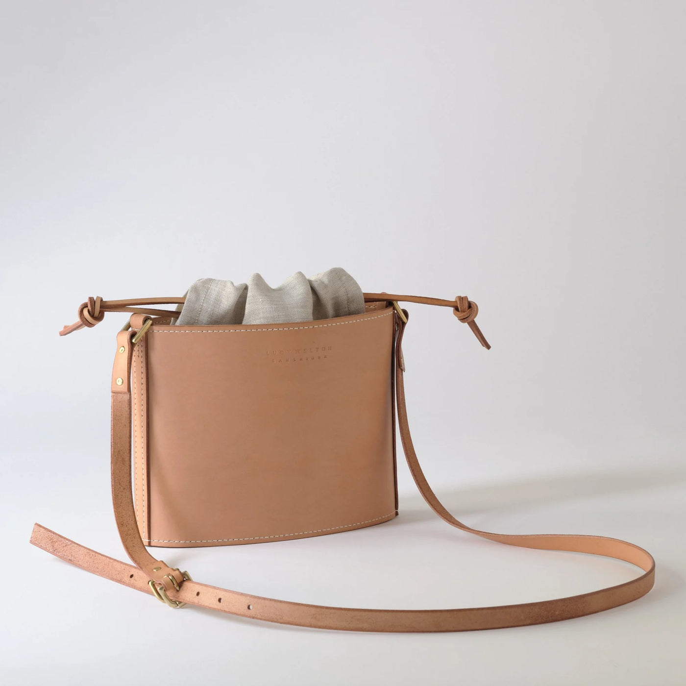 Tan leather crossbody bag with a strap on a light gray background