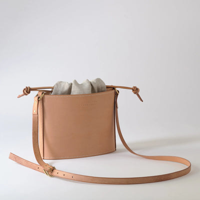 Tan leather crossbody bag with a strap on a light gray background