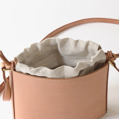 Tan leather handbag with a light gray interior lining on a white background