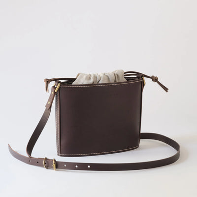 Brown leather handbag with a strap on a light gray background