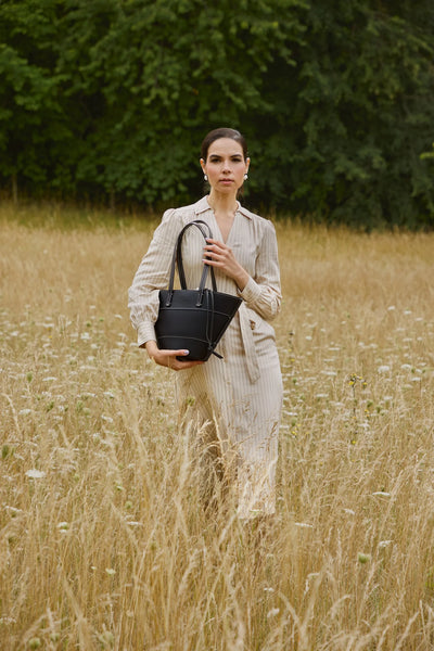 Woman holding a black handbag in a field with greenery in the background