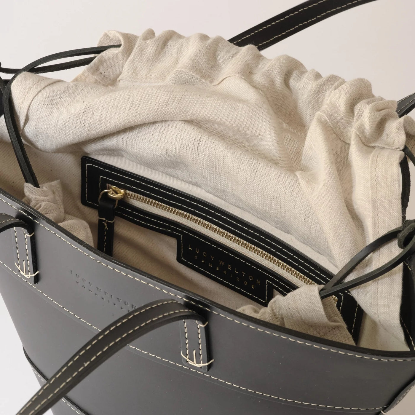 Gray handbag with beige interior lining and gold zipper detail on a light gray background
