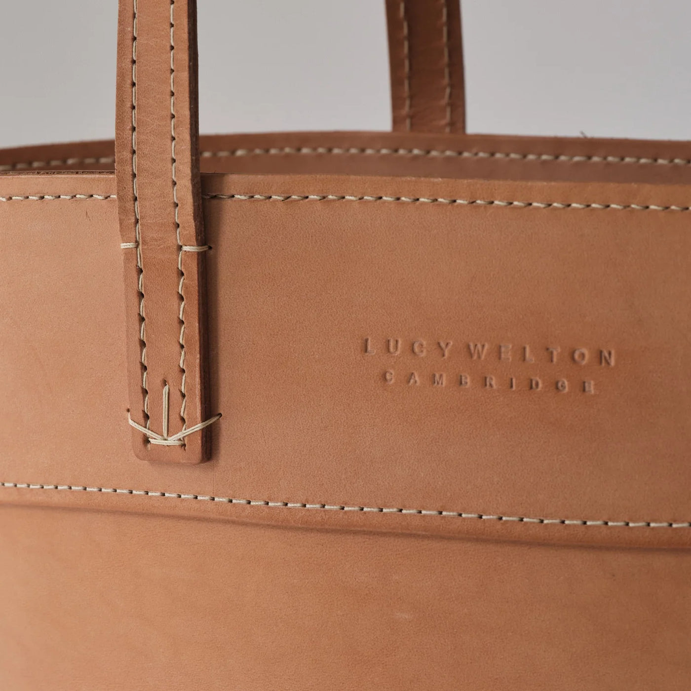 Close-up of a brown leather bag with visible stitching and 'Lucy Wilton Cambridge' branding.