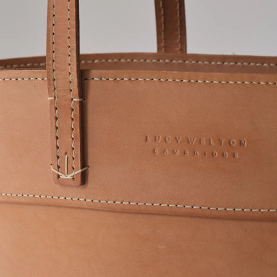 Close-up of a brown leather bag with visible stitching and 'Lucy Wilton Cambridge' branding.