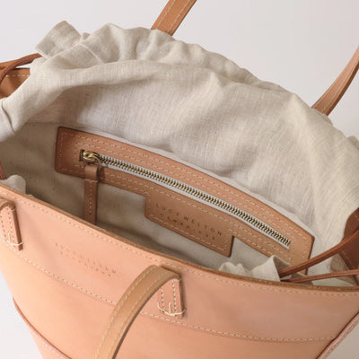 Close-up of a beige handbag with a visible brand name on a light gray background