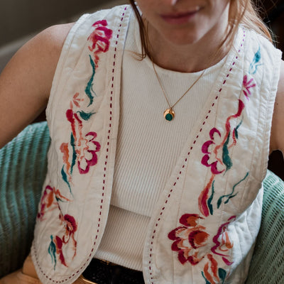 Person wearing a white embroidered vest with floral patterns over a beige top and pants.