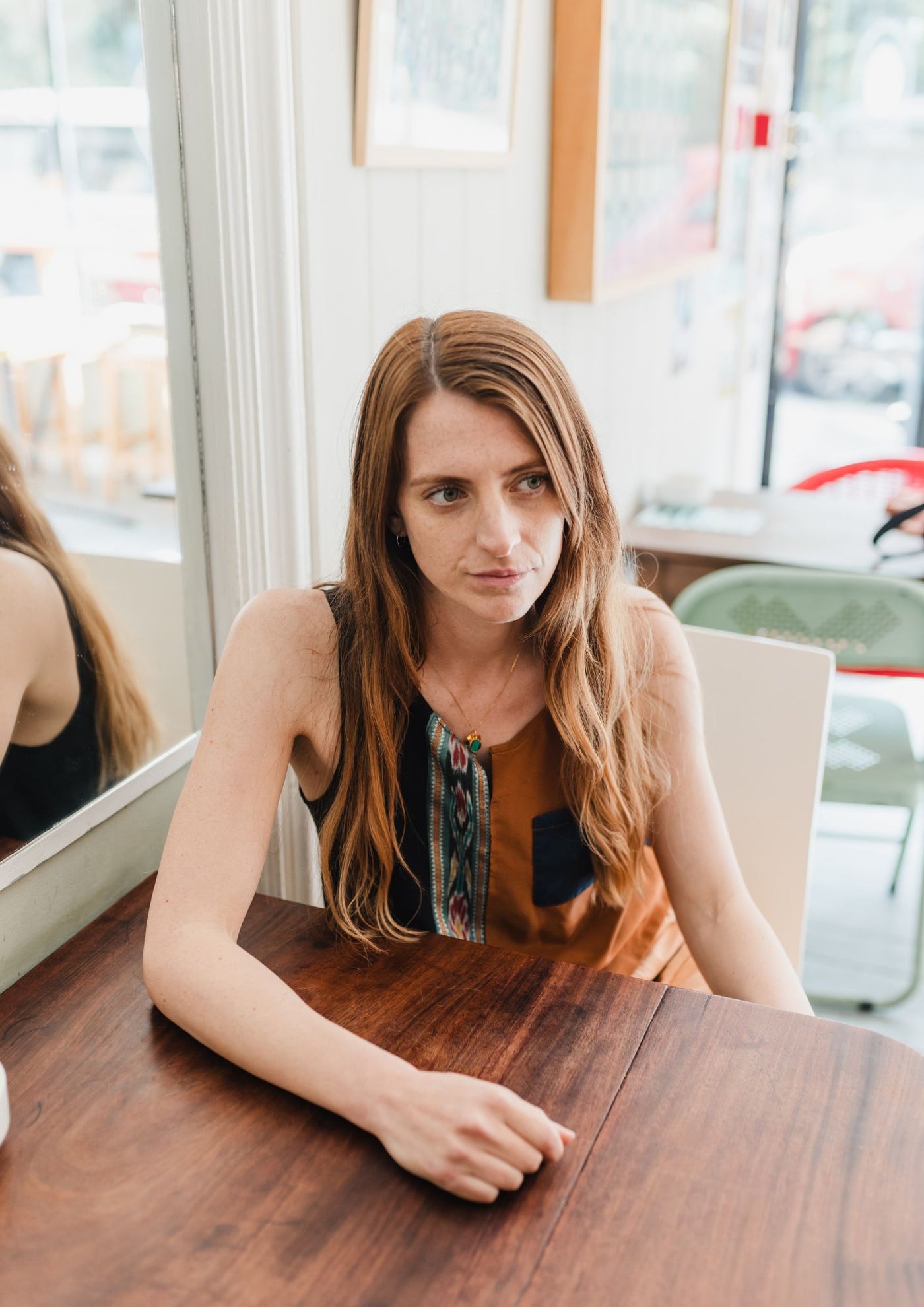 Woman sitting at a table in a casual setting with a mirror reflection.