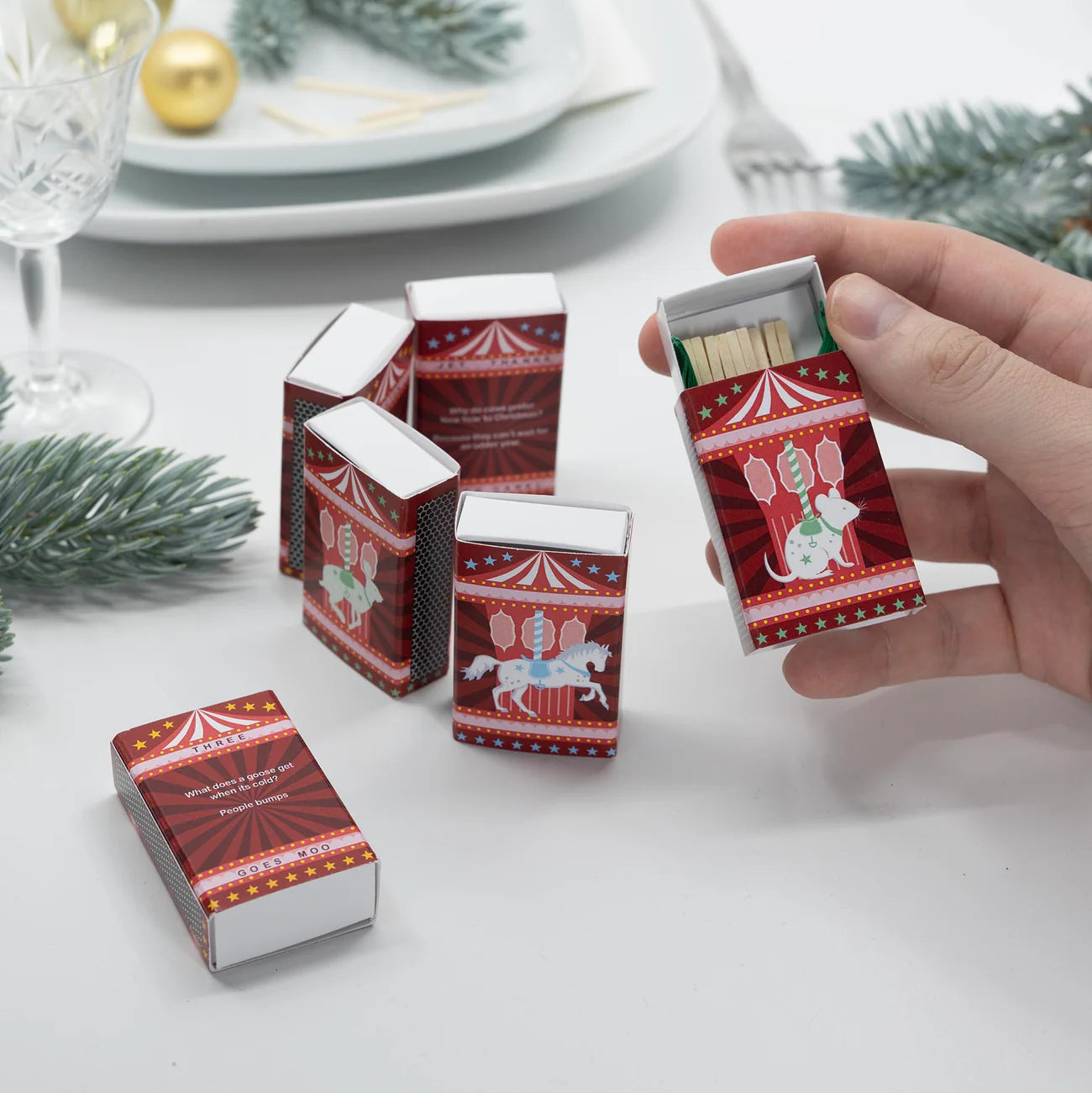 Decorative matchboxes with festive designs on a table with Christmas decorations.