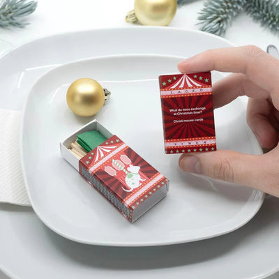 Red matchbox with green matches on a white plate, surrounded by Christmas decorations.