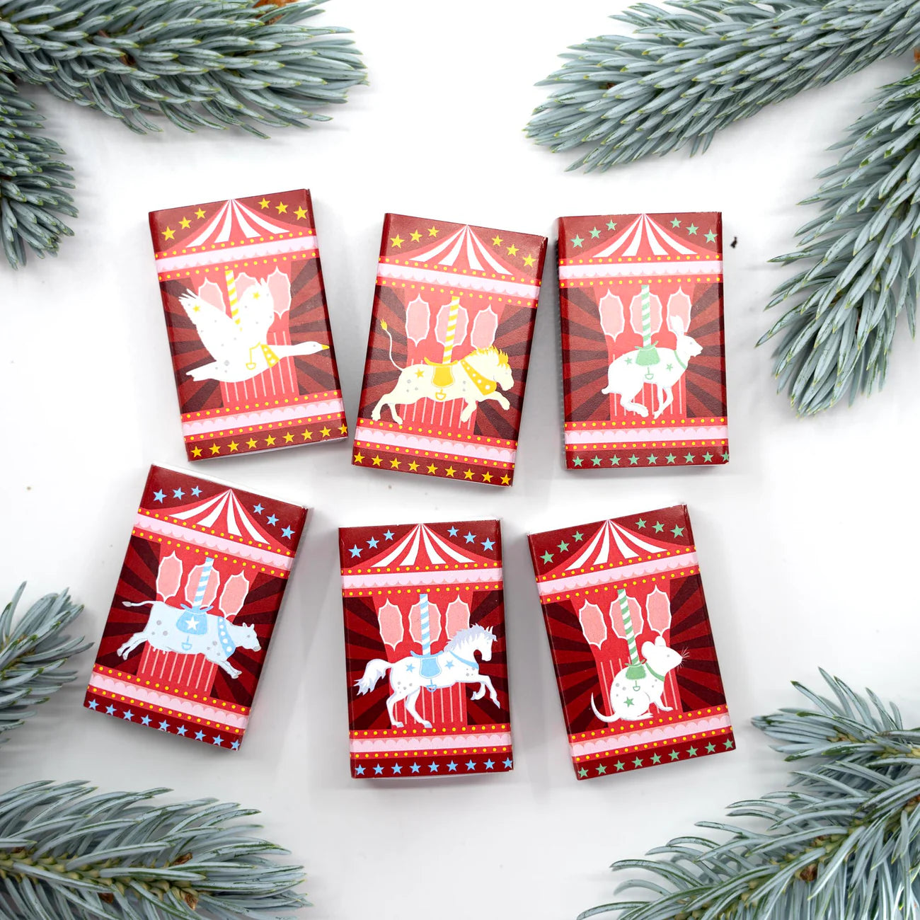 Six small red packages with carousel designs on a white background with pine branches.