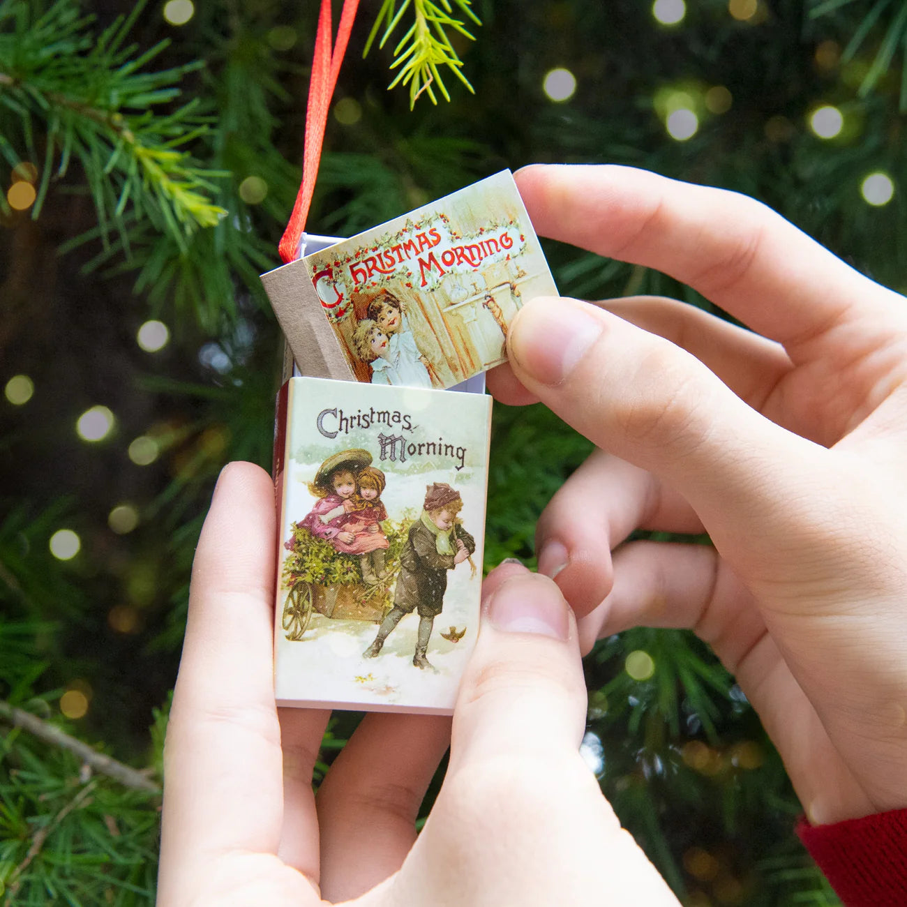 Miniature books titled 'Christmas Morning' held by a hand against a Christmas tree background.