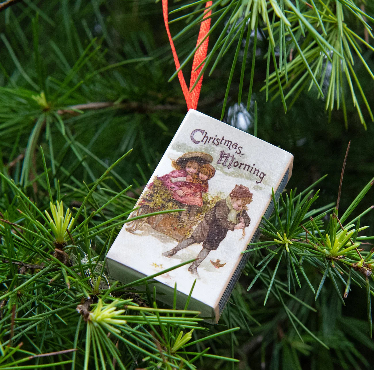 Decorative Christmas ornament with vintage illustration of two children on a pine branch.
