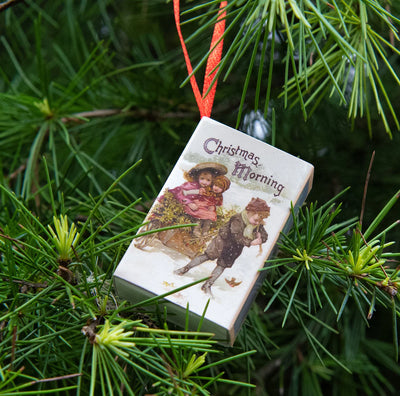 Decorative Christmas ornament with vintage illustration of two children on a pine branch.