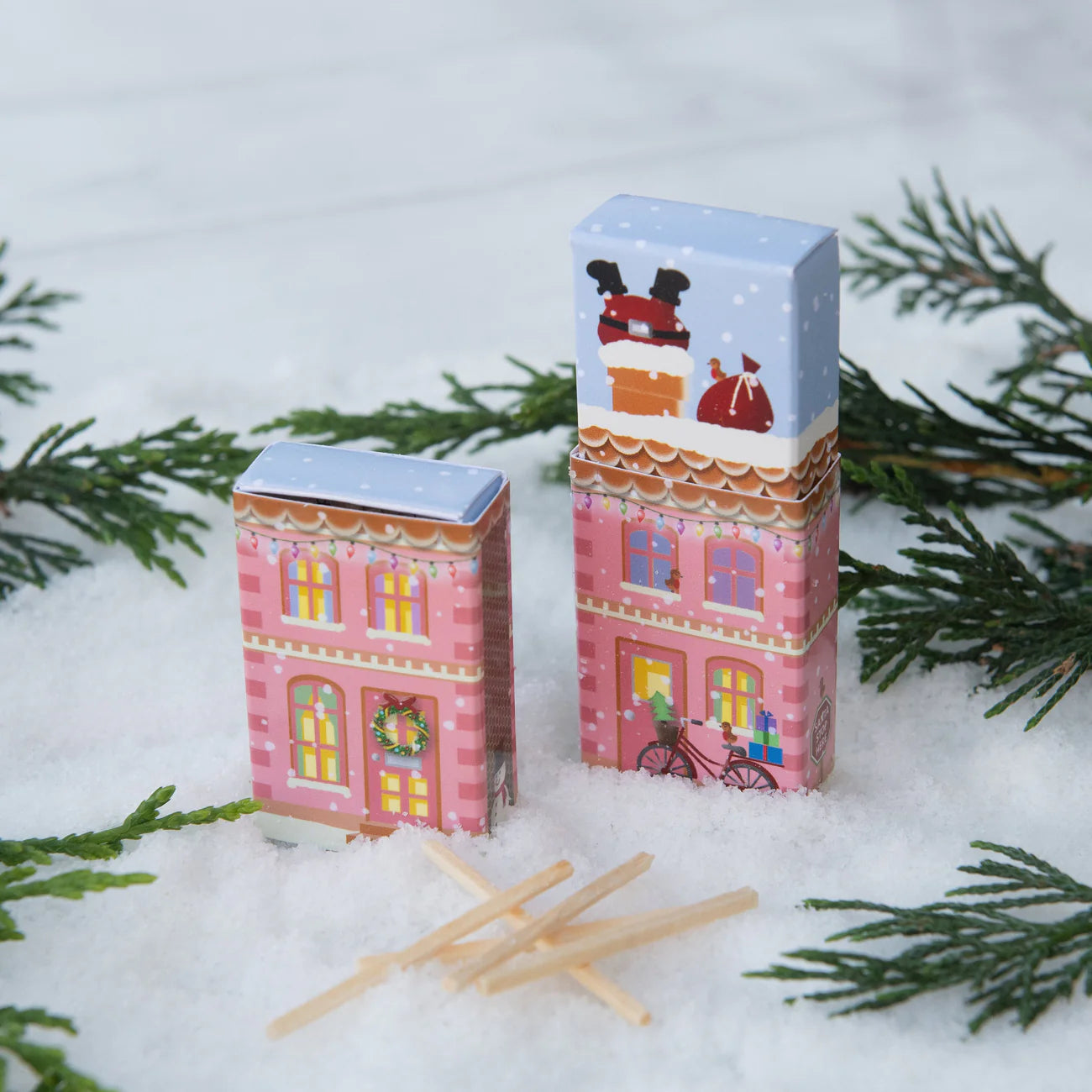 Two decorative matchboxes with festive designs on a snowy background