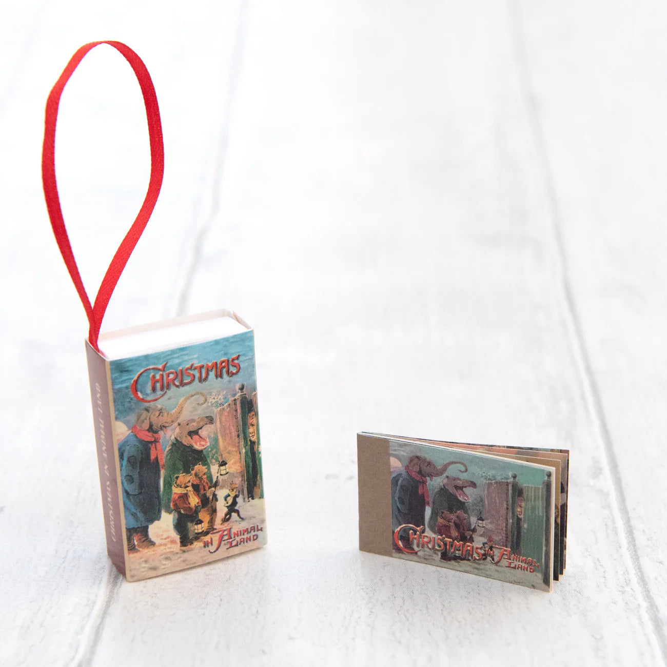 Christmas-themed book ornament with a red ribbon on a white background