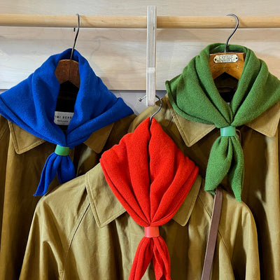 Three jackets with colorful scarves on hangers against a wooden wall.