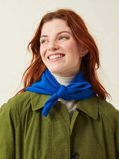 Woman wearing a green coat and blue scarf against a plain background