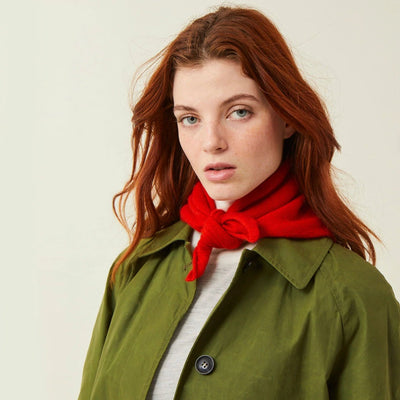 Woman wearing a green coat and red scarf against a plain background
