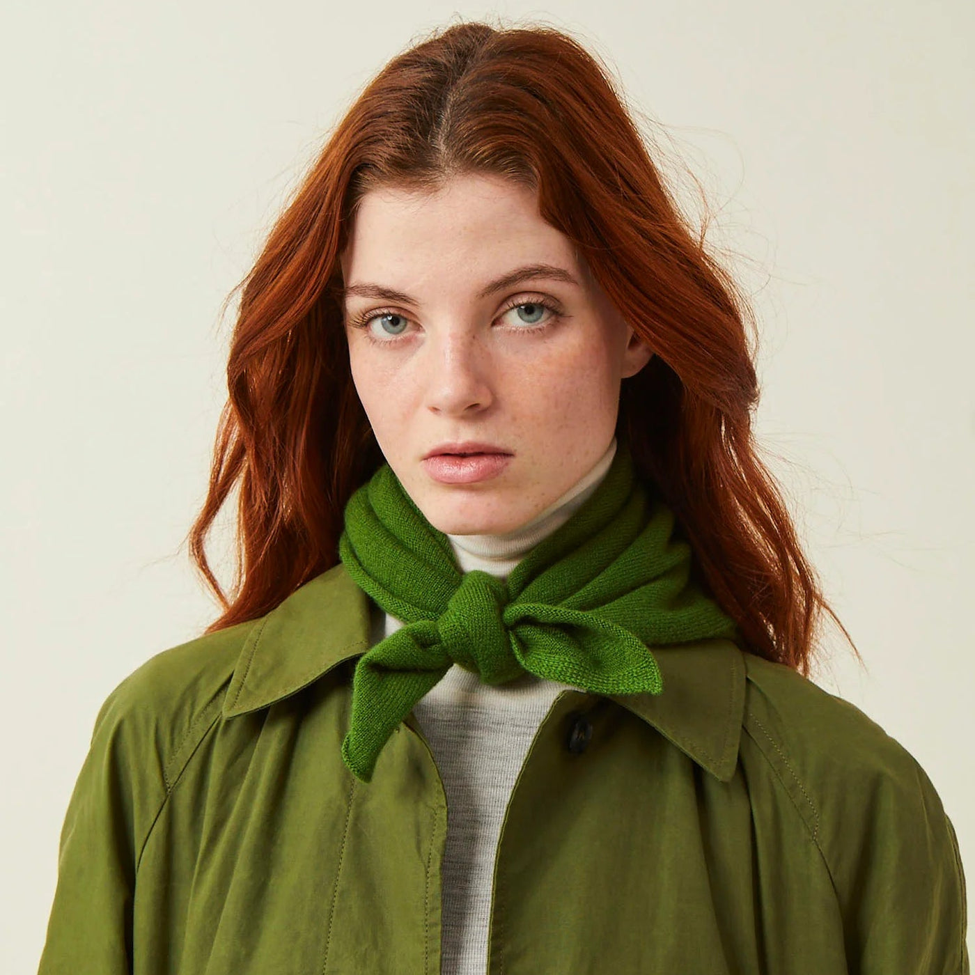 Woman wearing a green coat and green scarf against a plain background