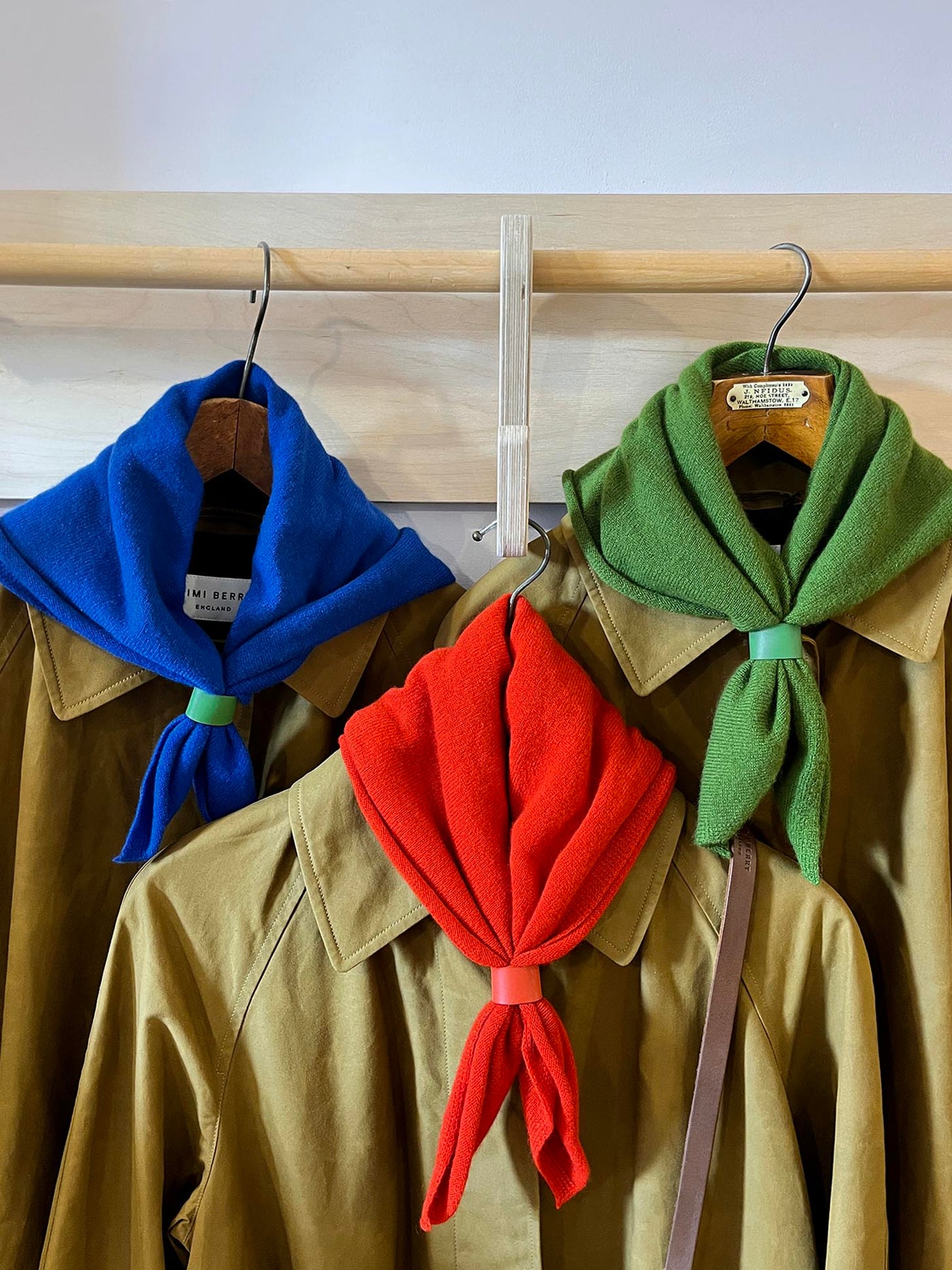 Three jackets with colorful scarves on hangers against a wooden wall.