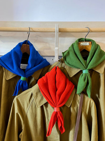 Three jackets with colorful scarves on hangers against a wooden wall.