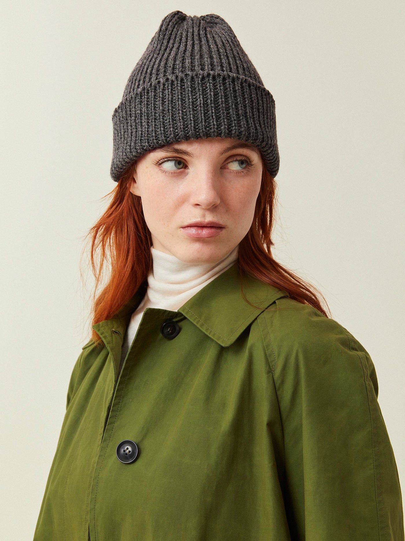 Person wearing a green coat and gray knit beanie on a plain background