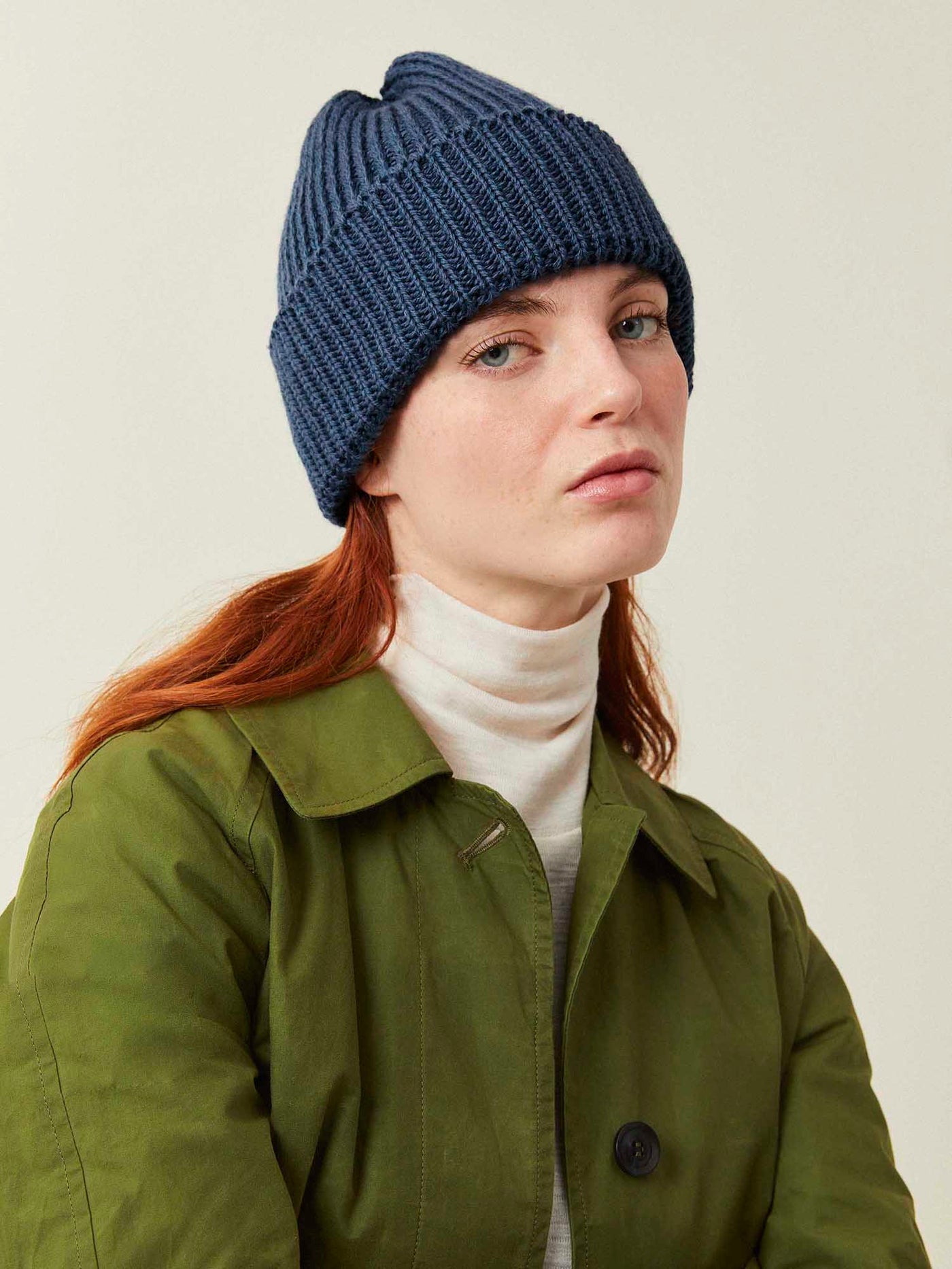 Person wearing a blue knit beanie and green jacket on a plain background