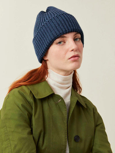 Person wearing a blue knit beanie and green jacket on a plain background