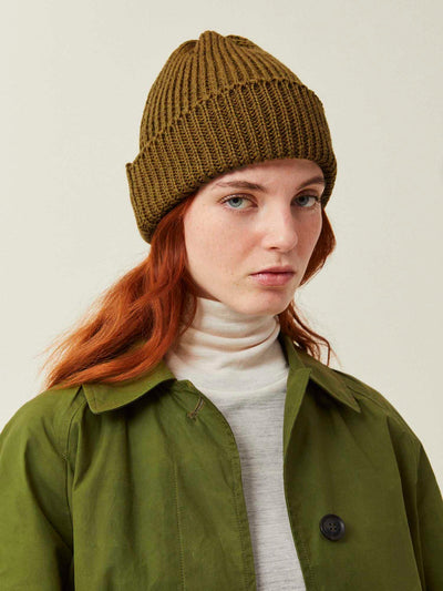Person wearing a brown knit beanie and green jacket on a plain background