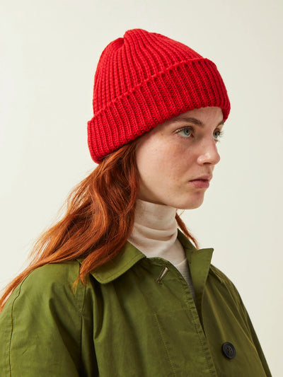 Person wearing a red knit beanie and green jacket on a plain background