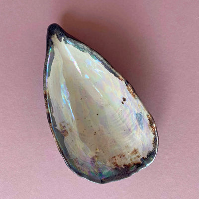 Teardrop-shaped stone with iridescent surface on a pink background