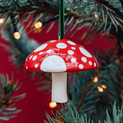 Mushroom-shaped Christmas ornament with red cap and white spots hanging on a tree.