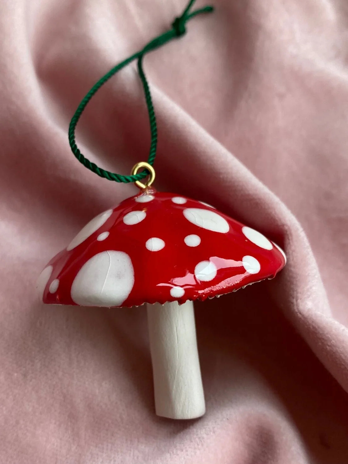 Mushroom-shaped ornament with red cap and white spots on a pink fabric background