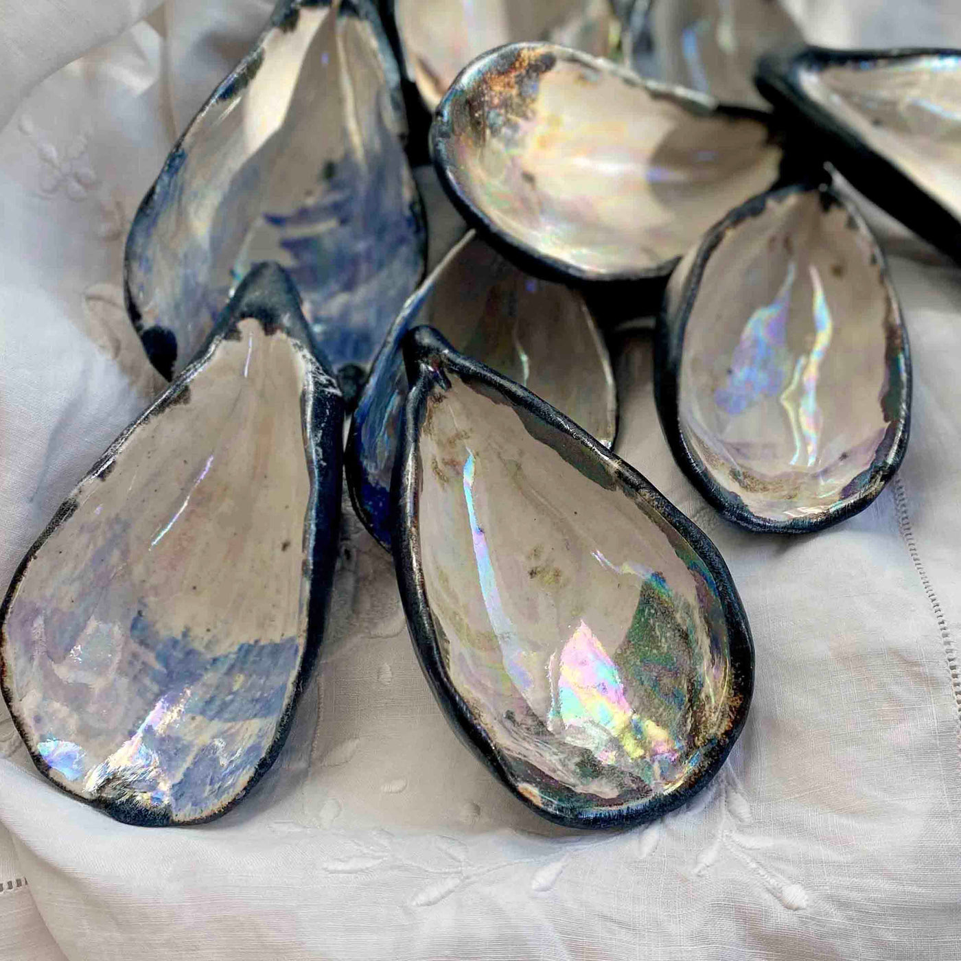 Teardrop-shaped shells with metallic interior on a white fabric background