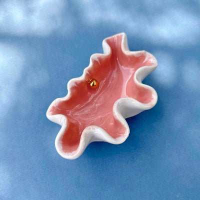 Pink leaf-shaped dish with a gold coin on a blue background