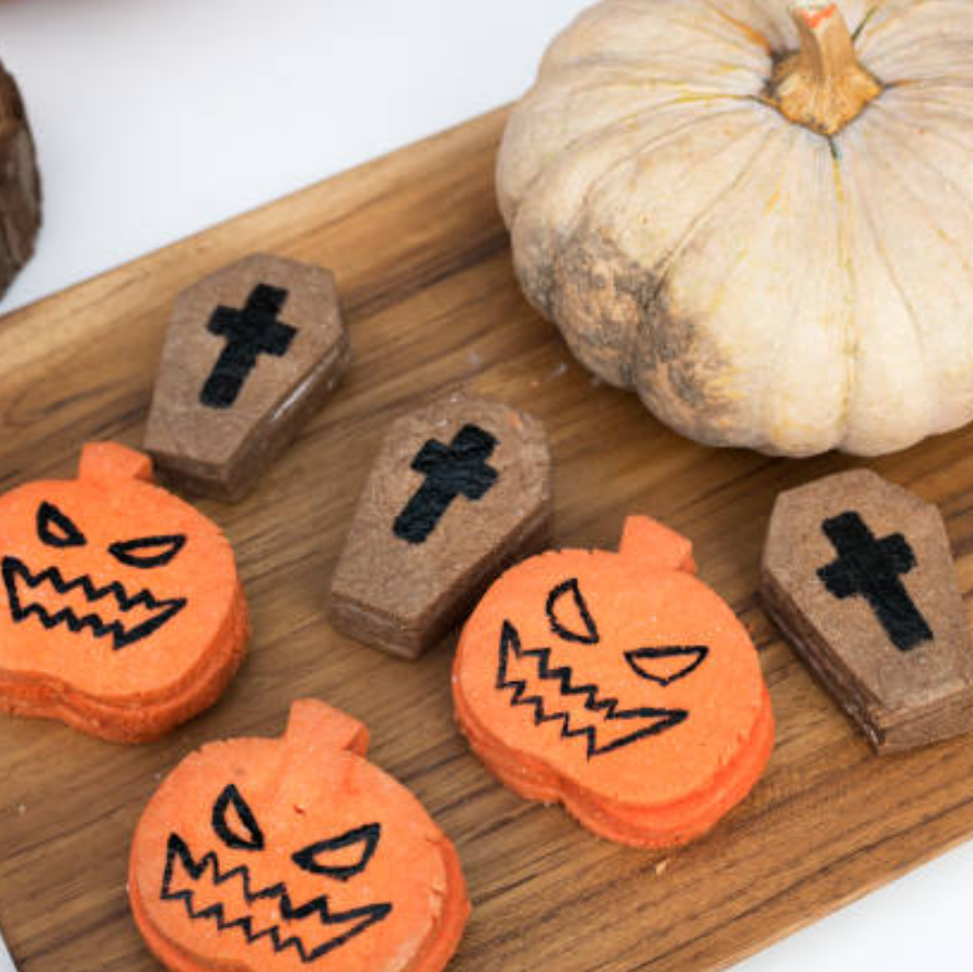 Halloween-themed cookies on a wooden board with a pumpkin and candle in the background.