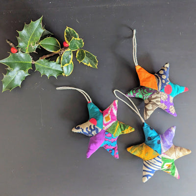 Colorful star-shaped fabric ornaments on a dark background with holly leaves.