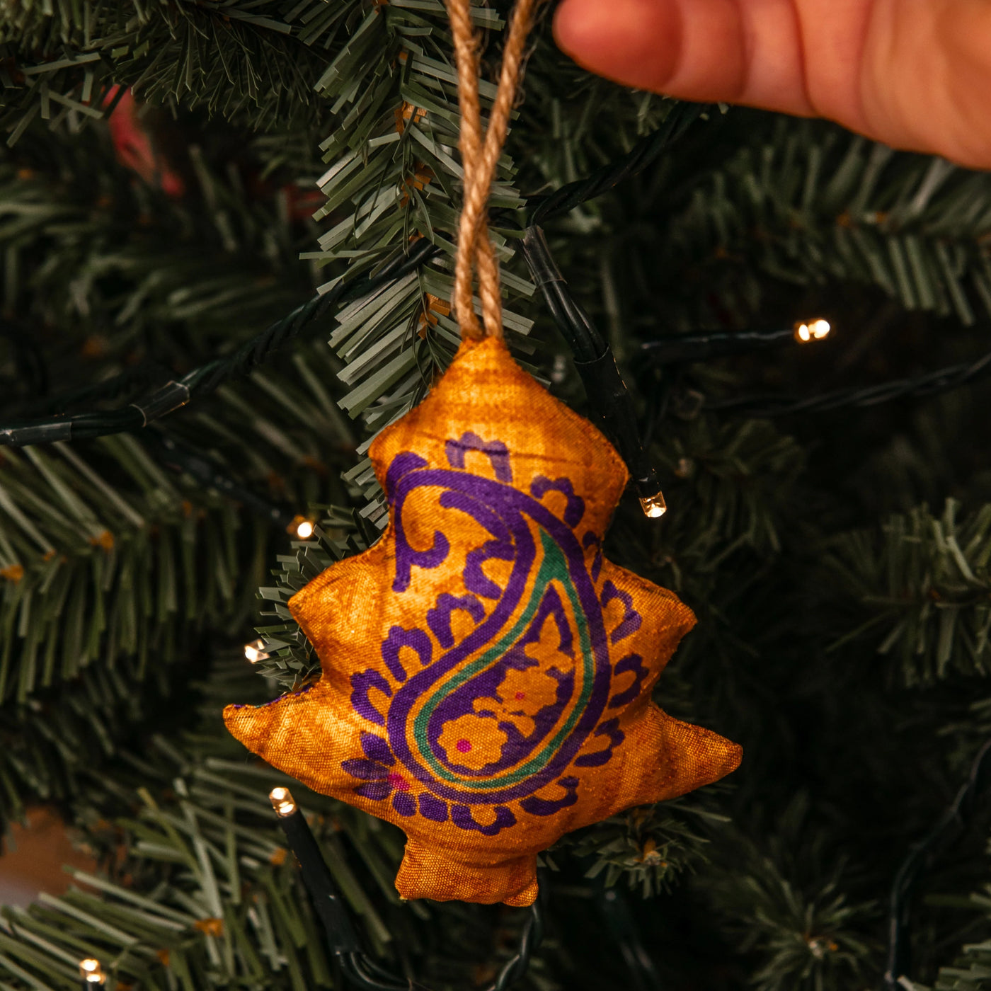 Star-shaped orange ornament with purple design on a Christmas tree