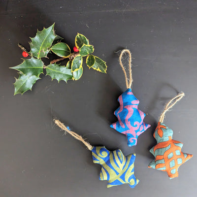 Colorful fabric ornaments and holly leaves on a dark surface