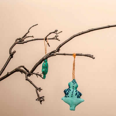 Two turquoise Christmas tree ornaments hanging from a branch against a beige background