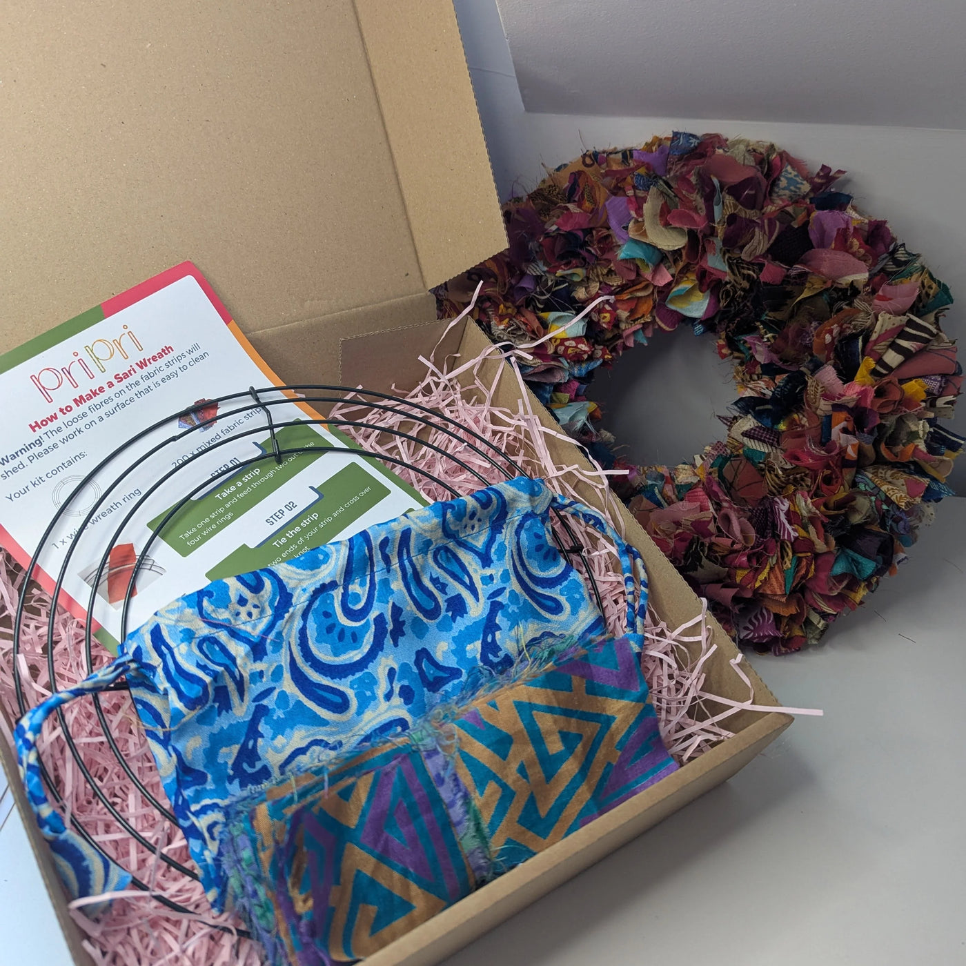 Box with fabric scraps, a wreath, and a pattern book on a white surface