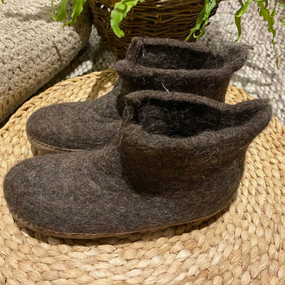 Pair of brown felted slippers on a woven mat with a plant in the background