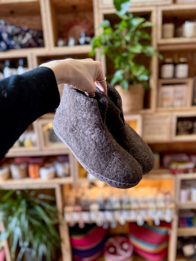 Person holding a pair of gray slippers in a store setting with shelves and plants.