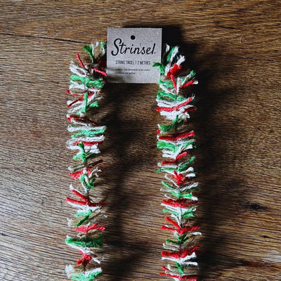 Decorative string with red, green, and white pattern on a wooden surface, branded 'Strinzel'.