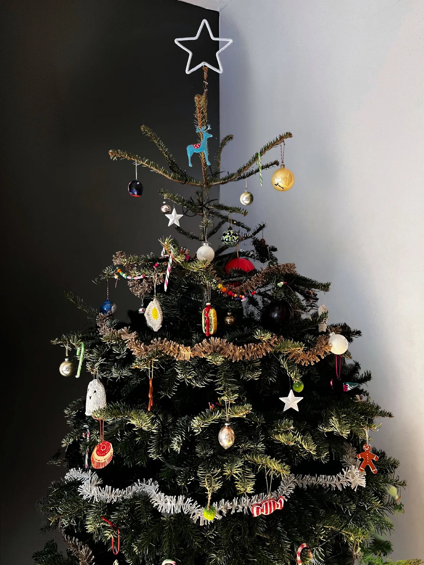 Decorated Christmas tree with various ornaments against a plain wall.
