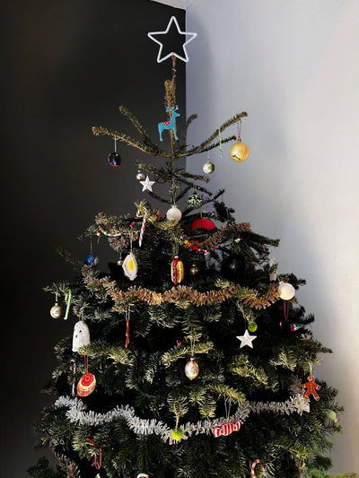 Decorated Christmas tree with various ornaments against a plain wall.