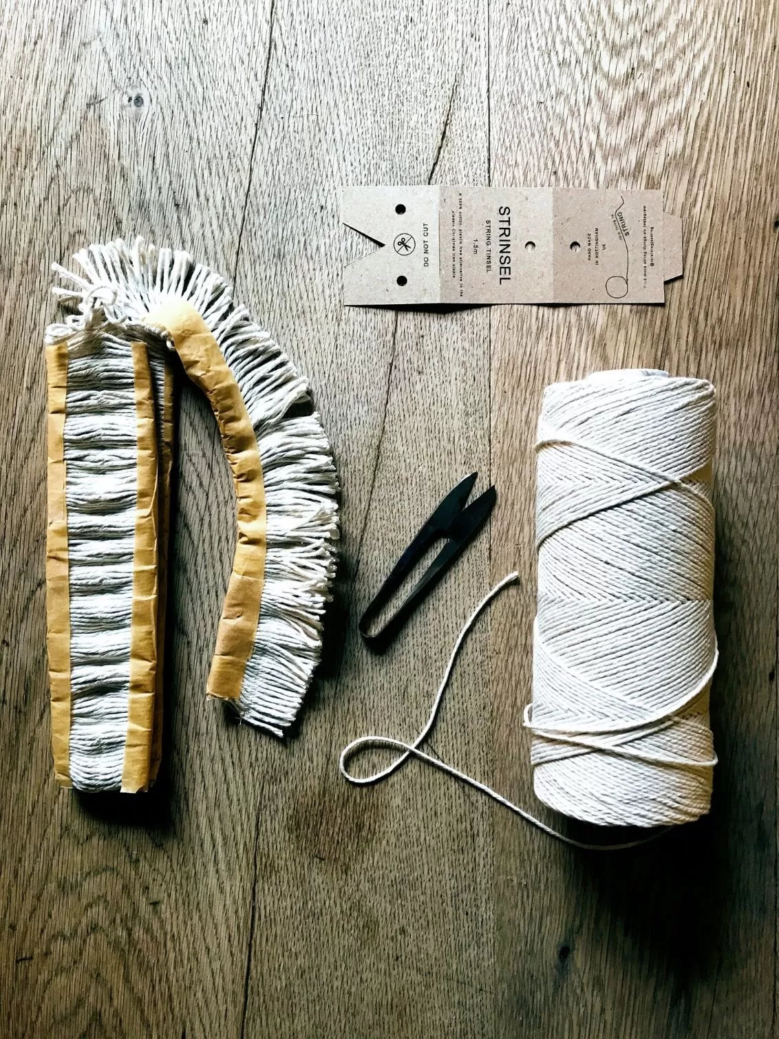 Decorative item with fringe, a spool of thread, and a label on a wooden surface